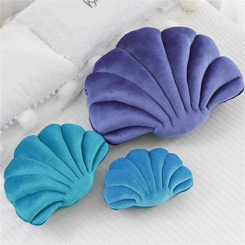Two velvet stuffed sofa cushions shaped like decorative seashells in purple and teal colors.