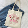 A beige canvas shopping bag featuring a pink cherry design, placed on a blue denim shirt.