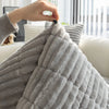 A close-up of a gray quilted flannel sofa pad cover being held by a hand.