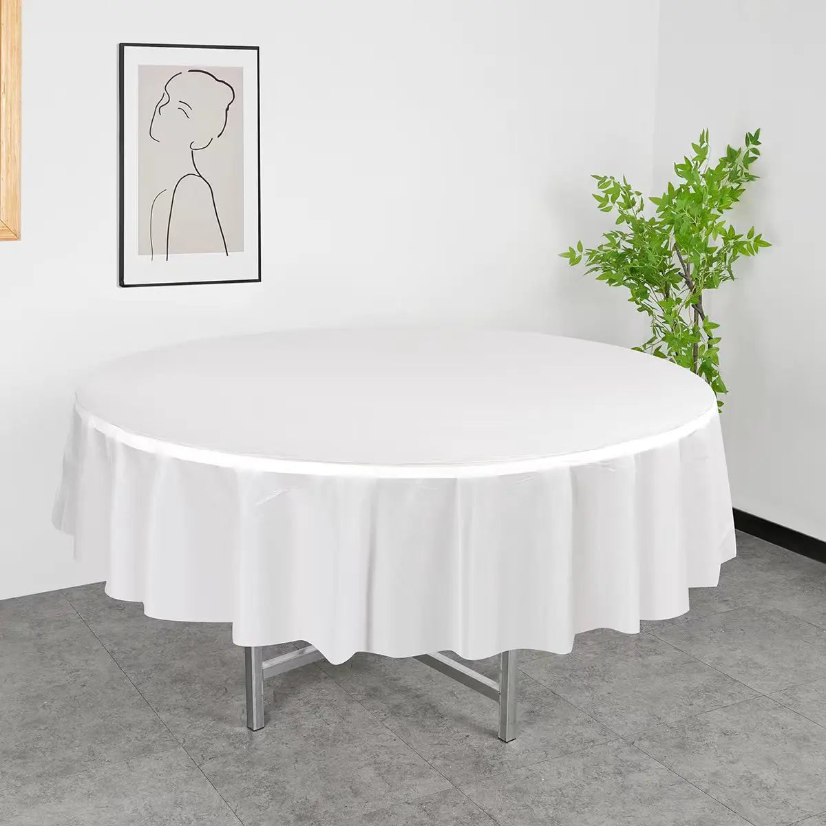 A round white plastic disposable table cover set displayed on a gray floor with a framed artwork in the background.