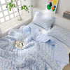 Light blue floral quilt set with matching pillows and a quilted blanket displayed on a white shelf.