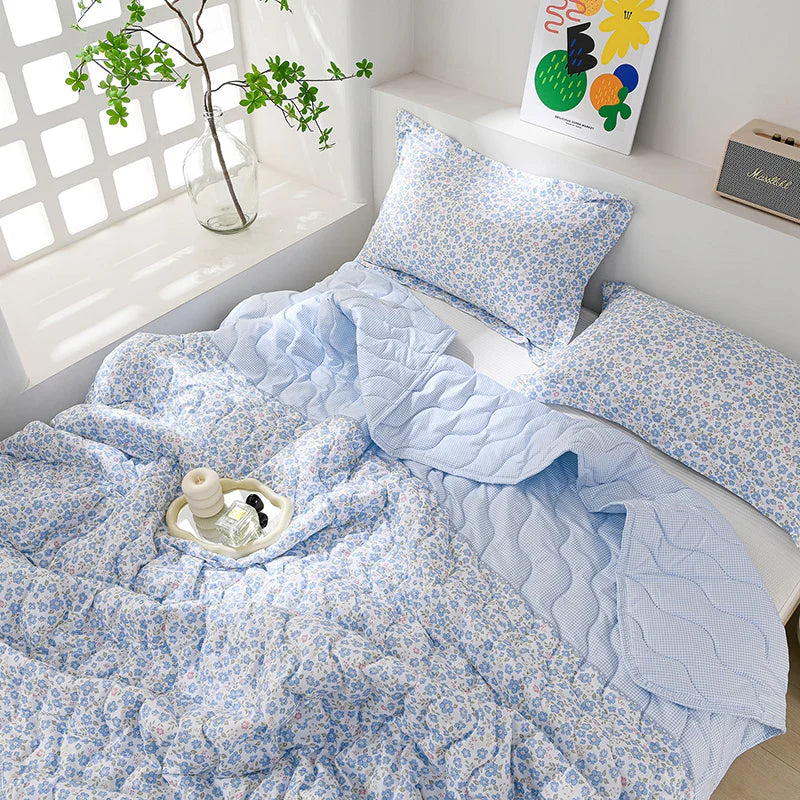 Light blue floral quilt set with matching pillows and a quilted blanket displayed on a white shelf.