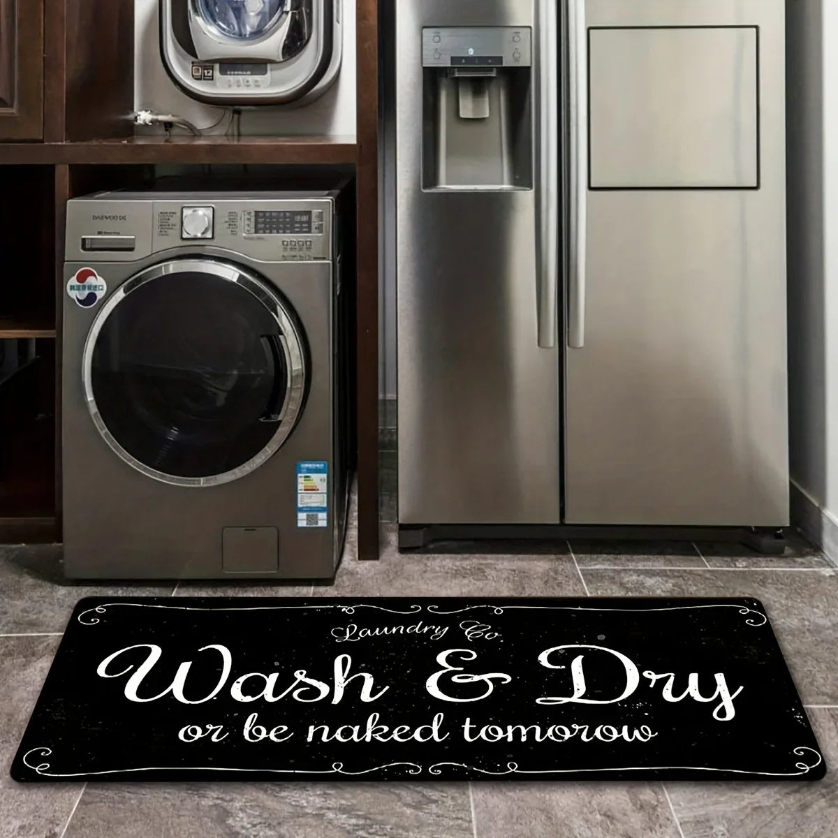 A black laundry mat with white text that reads Wash & Dry or be naked tomorrow placed on a tiled floor.
