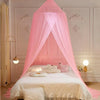 Pink sheer dome mosquito net draped over a bed with white bedding and decorative wall panels.