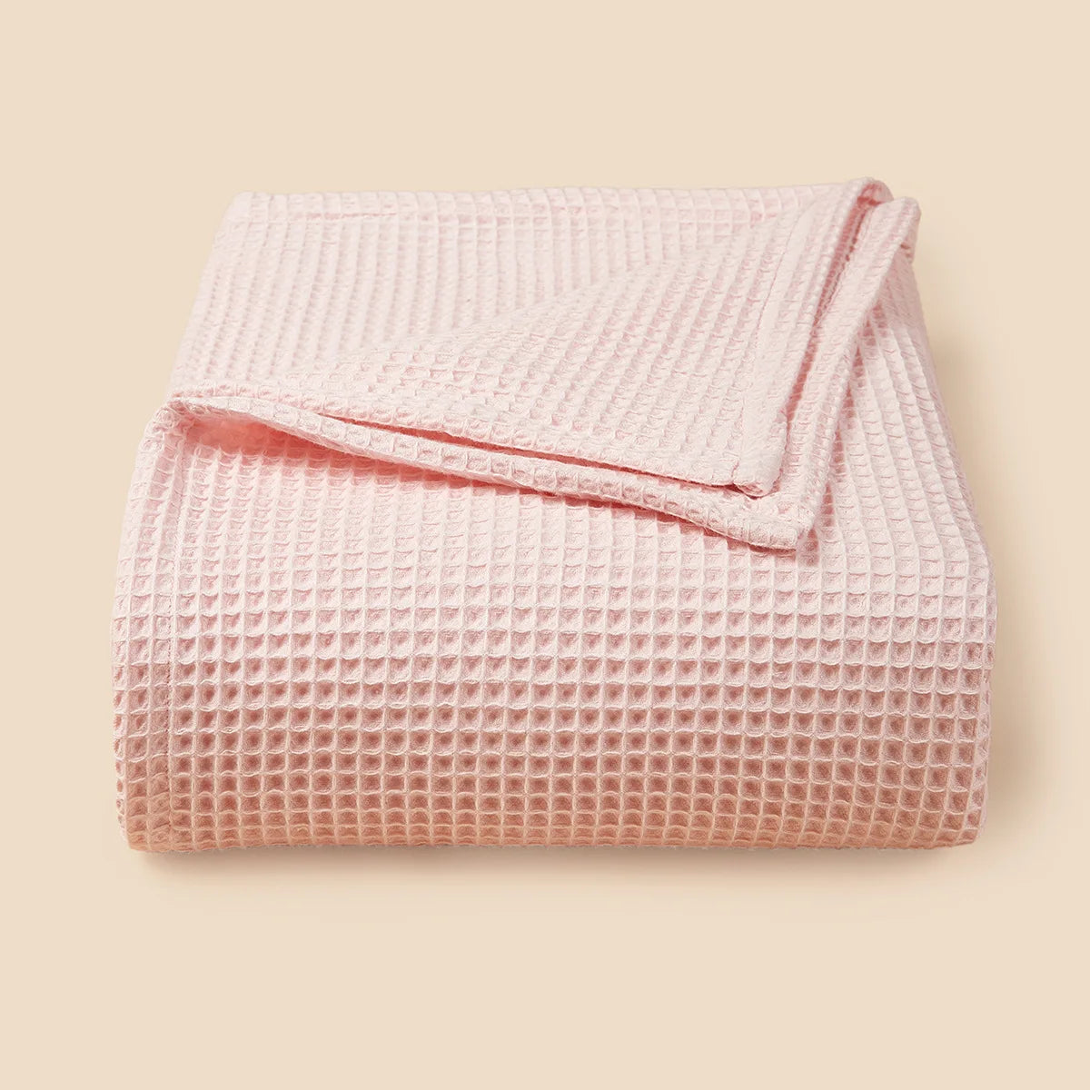 A pink lightweight cotton waffle blanket folded neatly on a neutral background.