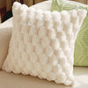 A white, textured plush pillow with a dimpled pattern resting on a light-colored surface.