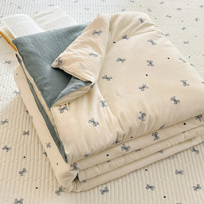 A beige cartoon quilting comforter with small blue butterfly patterns is folded on a white quilted surface.
