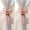 Two sets of pink sheer ribbon bow curtain tiebacks tied on white drapery.