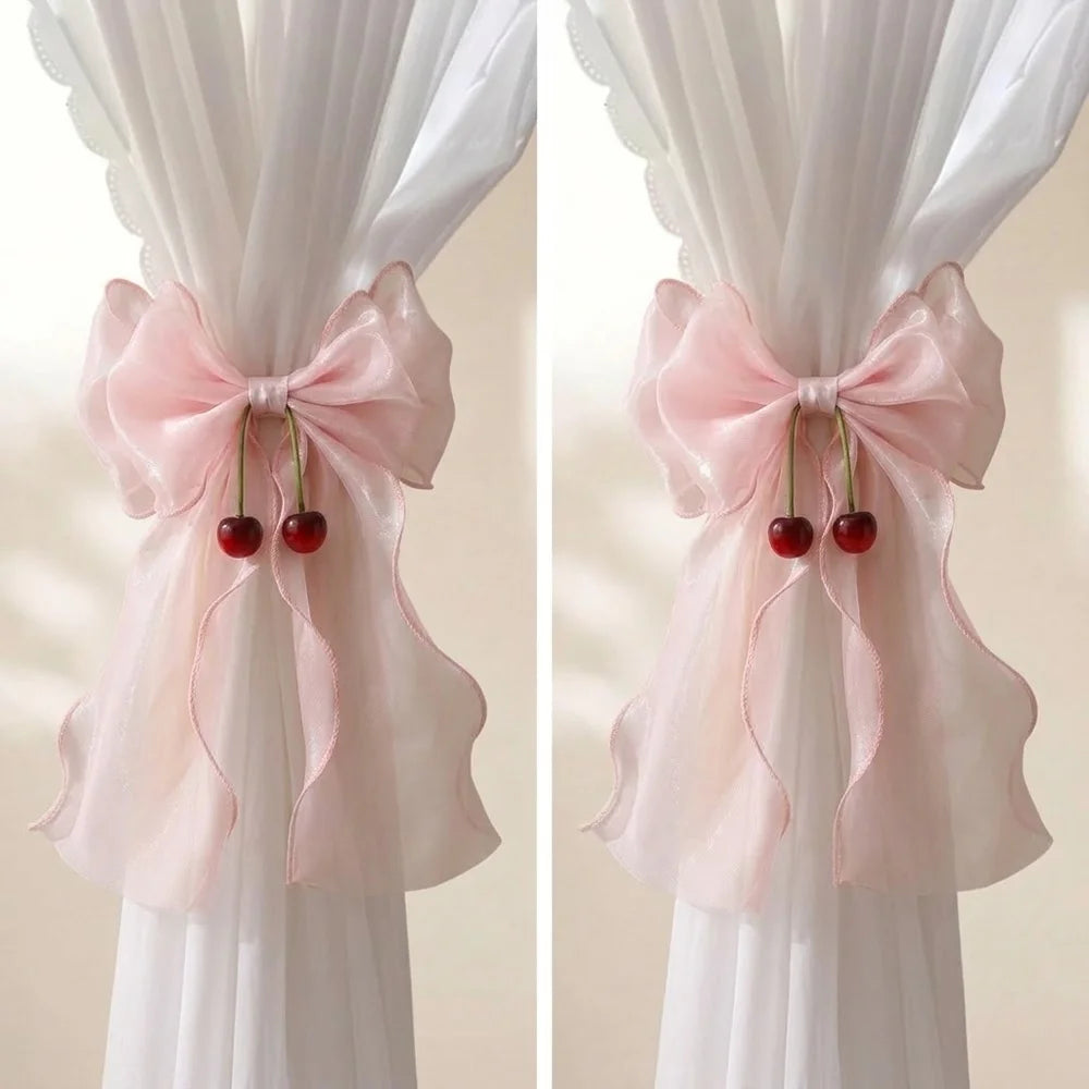Two sets of pink sheer ribbon bow curtain tiebacks tied on white drapery.