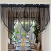 A sheer black beaded curtain with tassels hangs over a dining table in a bright room.