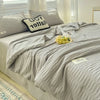 A light gray Korean style seersucker summer quilt set displayed on a bed with white and striped pillows.