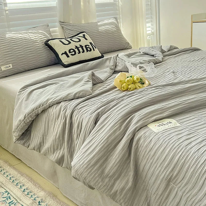 A light gray Korean style seersucker summer quilt set displayed on a bed with white and striped pillows.