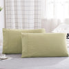 Two solid olive green microfiber pillow covers lying on a light gray bed.