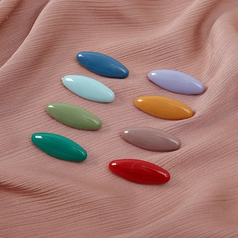 Eight plastic safety pins in various pastel and bright colors arranged on a pink fabric.