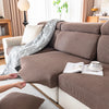 A close-up of a brown plush elastic sofa cushion cover with a patterned throw draped over it.