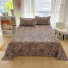 A flat bed with red floral print sheets is displayed in a bright room next to a white shelf and a white armchair.