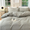 A bed dressed with a plaid duvet cover and matching pillowcases in shades of gray and white.
