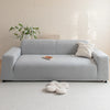 A light gray jacquard velvet sofa cover displayed on a white floor with a small decorative plant and cushion.