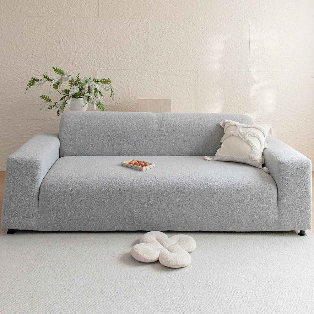 A light gray jacquard velvet sofa cover displayed on a white floor with a small decorative plant and cushion.