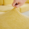 A hand is adjusting a yellow stretchable chenille sofa cushion cover.