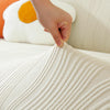 A hand is touching a white, ribbed stretchable sofa cover with a line pattern on a white couch.