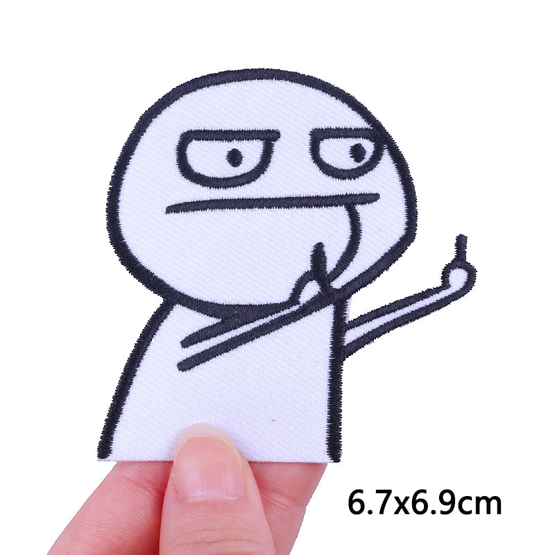 A white embroidered patch of a cartoon cat character making a gesture, shown being held by a finger.