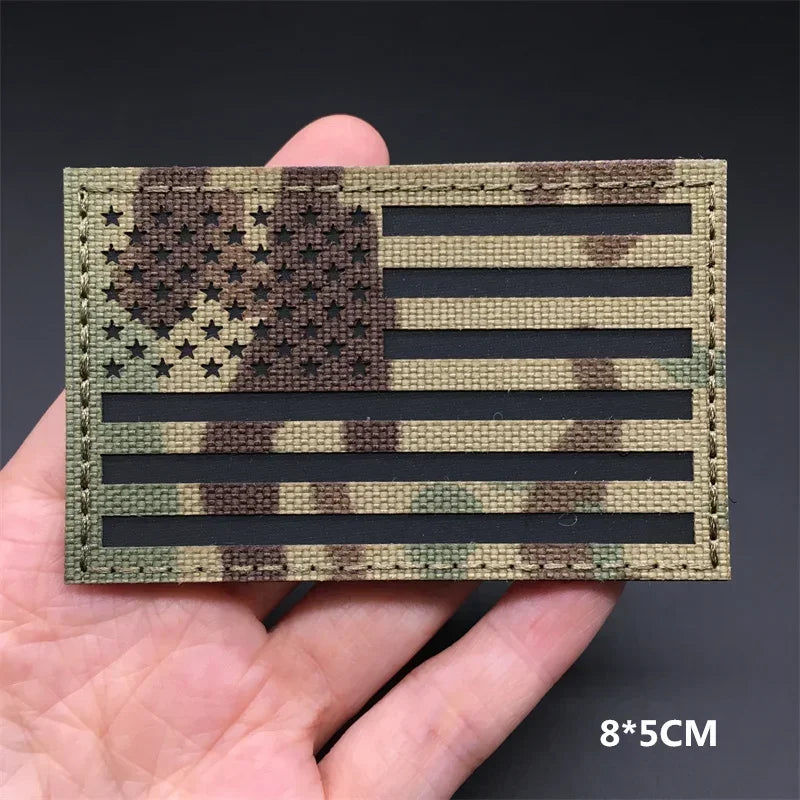 A rectangular fabric patch featuring a distressed American flag design in camouflage colors.