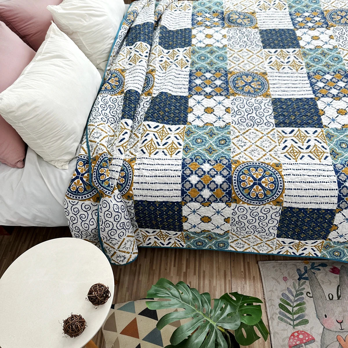A patterned pastoral embroidered cotton quilted bedspread displayed on a bed with white pillows and a wooden floor.
