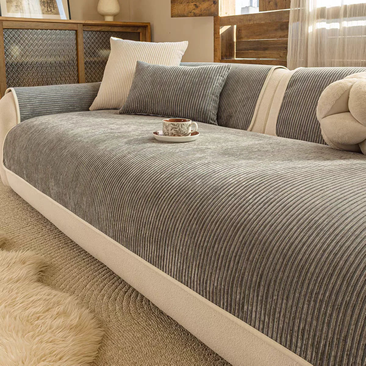 A beige striped slipcover sofa with gray and cream pillows and a fluffy rug.