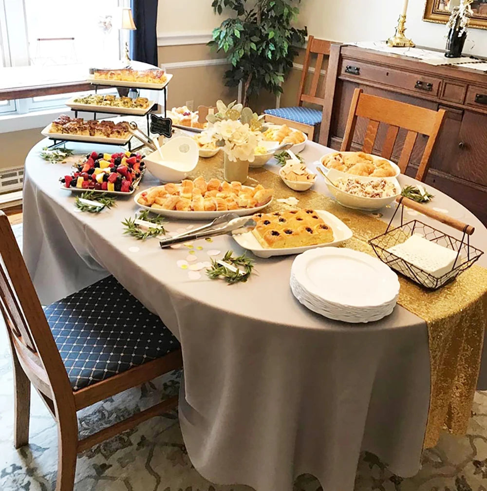 A long table set for a celebration featuring a gold sequin table runner and various appetizers.