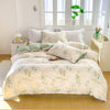 A white duvet cover set with a floral pattern featuring green and beige leaves displayed on a bed near a window.