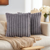 A set of two gray faux fur decorative pillows with vertical stripes resting on a light-colored sofa.
