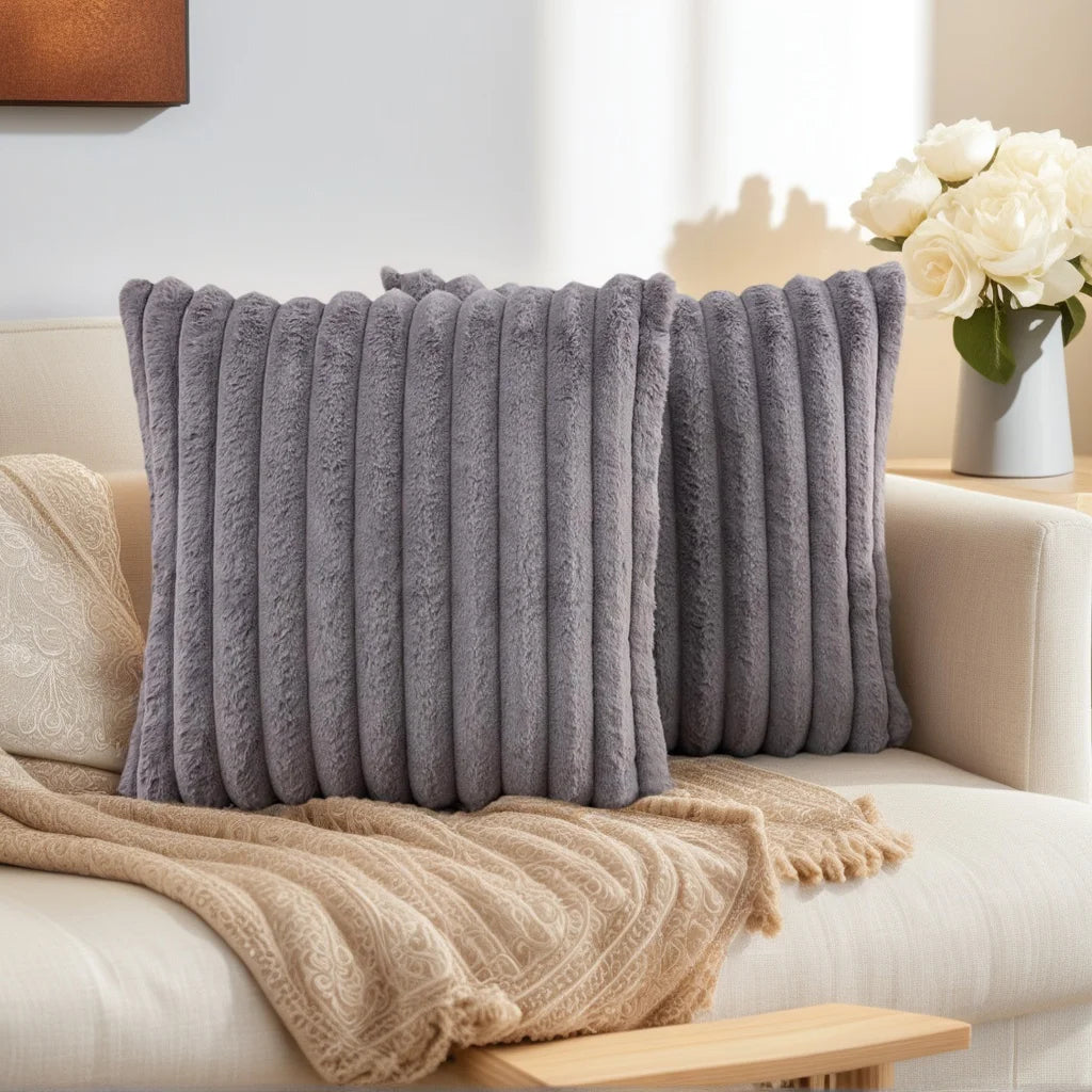 A set of two gray faux fur decorative pillows with vertical stripes resting on a light-colored sofa.