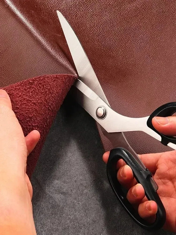 A pair of silver fabric scissors is shown cutting through brown leather material.