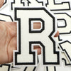 A hand holds a black and white letter patch shaped like the letter R for clothing decoration.
