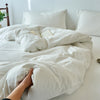 A hand is pulling the duvet cover of a white bed, revealing an open book inside.