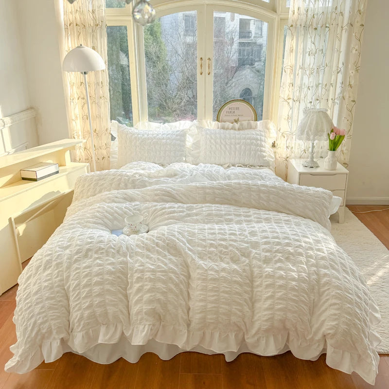 A white lace seersucker duvet cover set displayed on a bed with sheer curtains and a large window view.