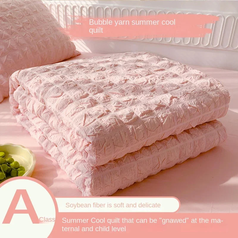 Pink bubble yarn summer cool quilt stacked on a surface with a bowl of green seeds.