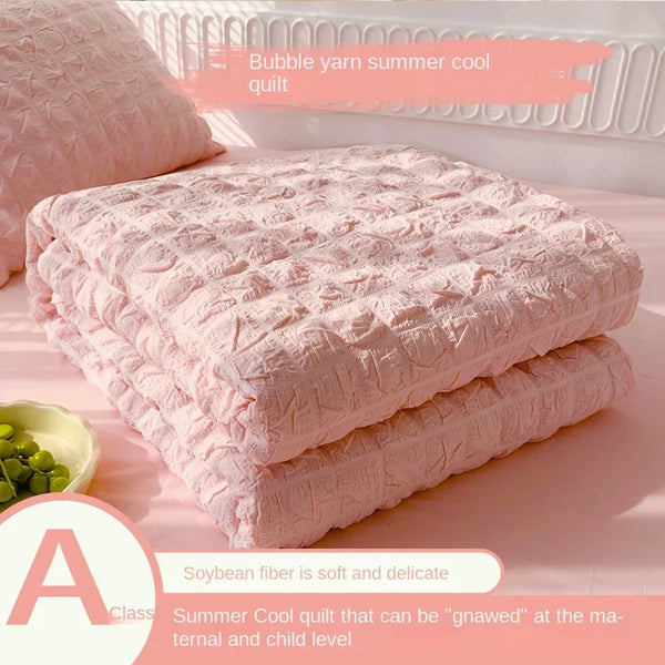 Pink bubble yarn summer cool quilt stacked on a surface with a bowl of green seeds.