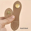 A set of eight handmade leather bag buttons in a tan color with gold accents shown being held by a hand.
