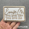 A beige embroidered patch with the text Enjoy Me you look like you love me is held in a hand.