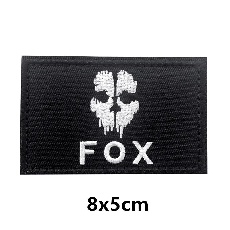 Black embroidered patch with a white fox head design and the text FOX on a dark fabric background