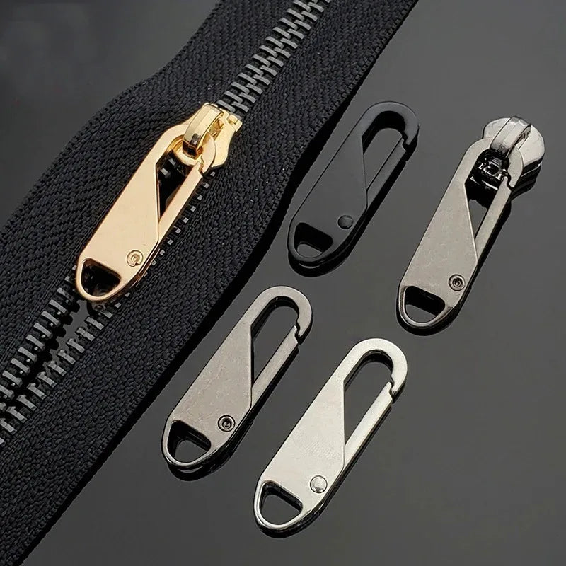 A set of brass and silver zipper pullers and a black zipper tape are displayed on a dark surface.