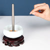 A hand uses a thin metal needle to thread a bead onto a stainless steel bead needle set for crafting.