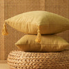 Two mustard yellow boho cotton linen throw pillows resting on a woven natural fiber surface.