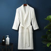 A white cotton terry robe hanging on a dark blue wall next to a potted green plant.