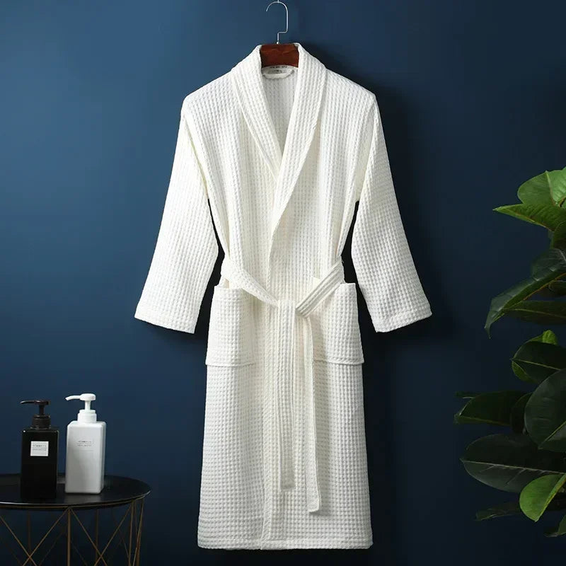 A white cotton terry robe hanging on a dark blue wall next to a potted green plant.