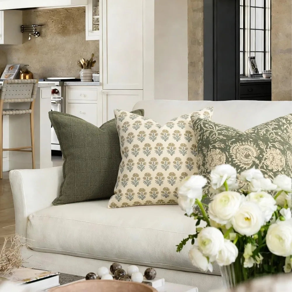 A white sofa decorated with various floral patterned throw pillows and a vase of white roses in a bright interior.