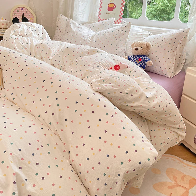 A collection of white and pink polka-dotted bedding, including a duvet cover and pillows, displayed in a bright room.