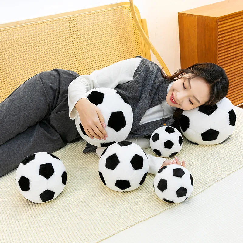 A woman is relaxing on a bed, holding and playing with a white football plush toy.